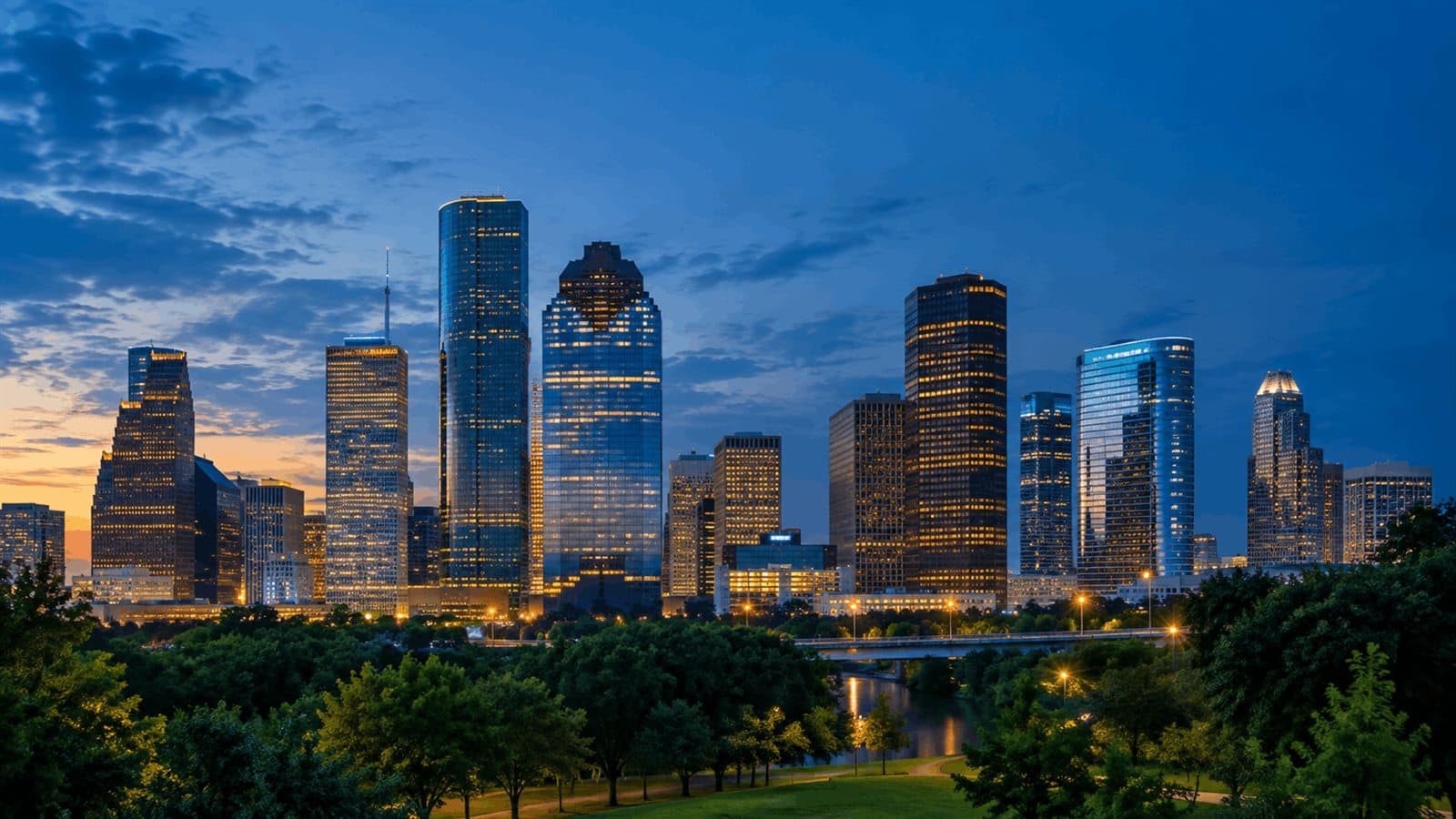 The downtown Houston skyline at dusk, lit office towers above a green park